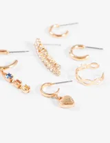 Set de seis aros de diferentes estilos en tono dorado, incluyendo aros tipo argolla, aros con dije de corazón, aros con dijes de cristales de colores y aros con tiras de strass colgantes.