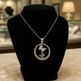 Dije circular de acero inoxidable con diseño calado de dos mariposas en el centro y detalle de guarda griega en el borde.