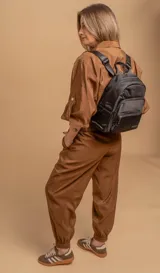 Mochila urbana de diseño funcional en color beige, confeccionada en tela impermeable. Cuenta con un compartimento principal amplio, un bolsillo secundario y un bolsillo frontal, todos con cierre. Incluye asa superior y correas ajustables para los hombros, con detalle de etiqueta de marca en el frente.