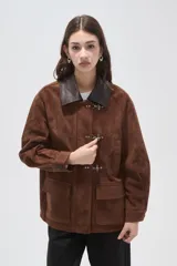 Chaqueta de gamuza color marrón con cuello camisero en cuero oscuro, cierre frontal con broches metálicos tipo gancho y bolsillos delanteros aplicados.