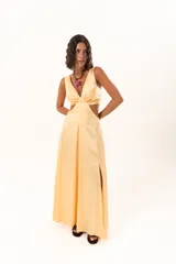 Vestido largo de tela sedosa color durazno, con escote en V, aberturas laterales en la cintura (cut-out) y tajos laterales en la falda. Posee espalda regulable con lazo y elástico.