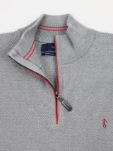 Buzo gris de hilo con cuello alto y medio cierre con cremallera roja.