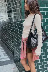 Bolso tipo maxi saca de cuero negro, con asa de hombro ajustable adornada con ojales metálicos plateados. Presenta cierre principal de cremallera y bolsillo interior con cierre.