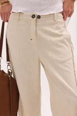 Pantalón de lino lavado color beige, de calce recto y diseño relajado. Presenta cintas de lino desflecadas aplicadas en los laterales con pespunte central, pretina con botón metálico, bolsillos delanteros y traseros.