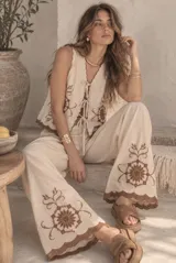 Conjunto de dos piezas color beige con bordados marrones, compuesto por un chaleco sin mangas con cierre de lazos frontales y un pantalón largo de corte amplio.