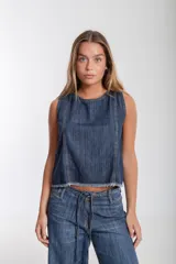 Blusa sin mangas de denim azul medio, con escote redondo y recortes verticales con costura expuesta en el frente. El ruedo inferior es deshilachado.