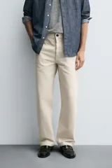 Pantalón chino de algodón color beige claro, corte recto, con cierre frontal de cremallera y botón, bolsillos delanteros y bolsillos traseros de doble vivo con botón.