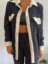 Camisa de pana negra con cuello, solapa, botones y bolsillos de parche en color crema. Corte recto y mangas largas.