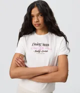 Remera de algodón con cuello redondo, mangas cortas y estampa en la espalda con diseño de un perro descansando en una reposera y la frase "Doing less is Self Care".