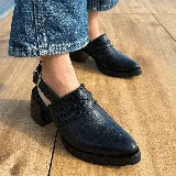 Zueco de cuero vacuno color negro, con diseño de tira trenzada en el empeine y cierre con hebilla metálica en el talón. Presenta punta fina y taco cuadrado de madera con acabado en cuero.