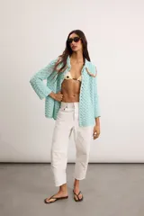 Saco de hilo de algodón tejido a crochet en color celeste, con diseño abierto, mangas largas y cuello romántico con detalles en tono tostado y cierre superior de botón.