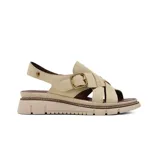 Sandalia plana Korium modelo Adamaris de color beige, confeccionada en gamuza con tiras cruzadas en el empeine, tira ajustable con hebilla metálica dorada y suela dentada en tonos beige y marrón.