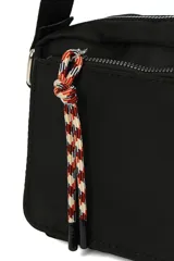 Bandolera de diseño rectangular en color negro, con cierre superior y bolsillo frontal con cierre. Incluye una correa larga ajustable para llevar al hombro o cruzada, y un detalle de tirador de cuerda trenzada en el bolsillo delantero.