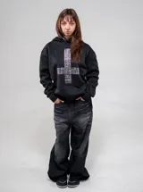 Buzo canguro negro con capucha, corte regular fit, de manga larga, con gran diseño de cruz frontal elaborado con tachas metálicas plateadas y tachas en el borde de la capucha.
