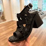 Sandalia negra de estilo gladiadora con tiras anchas texturizadas con efecto piel de serpiente. Posee un tacón bloque grueso y alto, y cierre de hebilla ajustable en el tobillo.