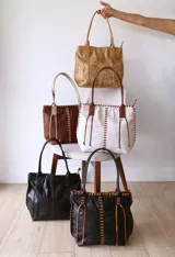 Cartera tipo tote de cuero color camel, con diseño artesanal que presenta costuras decorativas visibles en los laterales y el frente. Cuenta con doble asa de hombro y cierre superior.