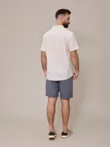 Camisa de manga corta para hombre, color blanco con rayas verticales finas en relieve. Tiene cuello abotonado, bolsillo en el pecho izquierdo y logo bordado pequeño.