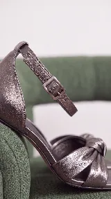 Sandalias de tacón medio ancho y puntera cuadrada, color peltre, con diseño de nudo frontal en las tiras y tira fina ajustable al tobillo con hebilla.