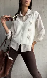 Chaleco tejido color natural con escote en V, diseño de trenzas y flores en relieve.