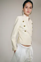 Chaqueta estilo militar ZW Collection confeccionada en hilatura con mezcla de algodón, color crudo, con cuello subido, manga larga, falsos bolsillos de vivo y cierre frontal con ganchos metálicos y botones decorativos dorados.
