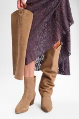 Bota de caña alta confeccionada en cuero vacuno, con diseño versátil que permite doblar la caña. Presenta un taco cuadrado de altura media y punta redondeada.