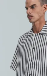 Camisa de manga corta con cuello abierto y calce oversize, confeccionada en sarga liviana con estampado de rayas verticales en negro y blanco.