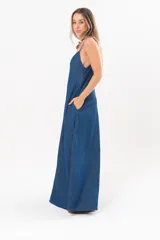 Vestido largo de denim fino y liviano, color azul, con breteles finos, escote en V y falda amplia con recortes verticales y bolsillos laterales.
