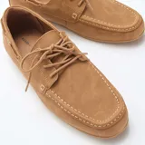 Mocasines náuticos de hombre en color tostado, confeccionados en material sintético con efecto gamuza. Presentan costuras visibles en relieve, cordones decorativos laterales y cierre frontal con cordones en el empeine.