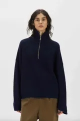 Sweater de punto color azul marino, con cuello alto, cierre frontal parcial y mangas largas anchas.