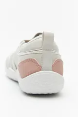 Zapatilla tipo guillermina de estilo barefoot, color beige con detalles en rosa pálido en el talón y tira de ajuste con velcro. Posee suela plana y flexible diseñada para un movimiento natural del pie.