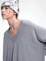Sweater de punto color gris, con escote en V profundo, hombros caídos y diseño holgado de corte relajado.