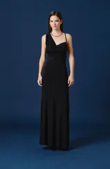 Vestido largo negro de corte sirena, con escote asimétrico tipo drapeado y un solo bretel fino. Presenta una silueta ajustada en el torso que se ensancha suavemente hacia el ruedo.