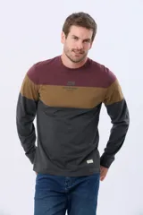 Remera de manga larga con cuello redondo y diseño de rayas horizontales en azul verdoso, beige y azul marino. Presenta una estampa frontal con texto y un parche decorativo en la manga.