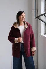Tapado de paño bordó con interior en color beige, diseño con capucha, cierre frontal y bolsillos laterales. Presenta costuras visibles y puños vueltos que dejan ver el contraste de color.