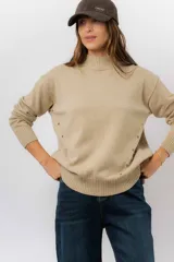 Sweater de tejido de punto color marrón, con cuello alto, corte relajado y terminaciones en rib en puños y cintura. Presenta una hilera de botones metálicos decorativos en uno de los laterales.