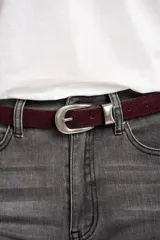 Cinto de cuero negro con textura de gamuza, presenta una hebilla metálica plateada de diseño clásico y puntera metálica a juego.