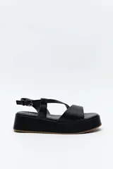 Sandalia negra con plataforma, tiras cruzadas sobre el empeine y pulsera ajustable al tobillo.