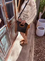 Cartera bandolera negra de cuero con forro interno de tela, detalle de flecos de cuero marrón en la parte inferior y asa larga regulable.