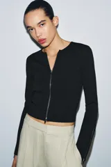 Chaqueta de punto liso color blanco, con cuello redondo, manga larga acabada con cremalleras en los puños y cierre frontal con cremallera.