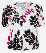 Blusa de viscosa con escote en V y mangas cortas abullonadas. Presenta un estampado de follaje y flores en tonos negro, fucsia y beige sobre fondo blanco.