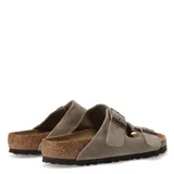 Sandalias Birkenstock modelo Arizona de dos tiras ajustables con hebillas metálicas. Confeccionadas en gamuza color taupe, cuentan con plantilla anatómica de corcho y suela de goma antideslizante.