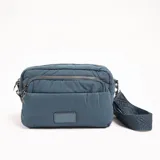 Bandolera azul acolchada con correa ancha estampada y cierre de cremallera.