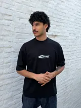 Remera negra de corte oversize con un pequeño gráfico ovalado en el pecho que contiene la palabra "OSTEN" en tipografía futurista.