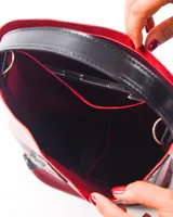 Matera tipo bucket de cuero color bordó, con detalles de tiras verticales en cuero negro adornadas con remaches metálicos plateados. Cuenta con un asa de mano fija y un compartimento interior amplio.
