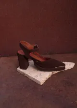 Sandalia de gamuza color marrón, con taco ancho, punta fina y tira ajustable al tobillo. Incluye detalle metálico en la puntera.