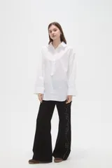 Camisa de algodón blanca de corte holgado, con cuello clásico, cierre frontal parcial con botones y mangas largas con puños anchos.