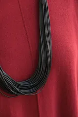 Collar largo de diseño artesanal compuesto por múltiples hilos negros finos que se unen en los extremos mediante secciones cilíndricas envueltas en hilo color beige.