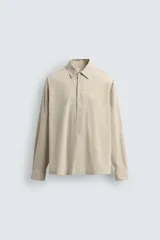 Camisa polo de corte relajado confeccionada en algodón, con estampado de rayas verticales finas. Presenta cuello solapa, cierre frontal parcial con botones, bolsillo plastrón en el pecho y mangas largas con puños abotonados.