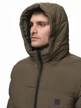 Campera puffer color verde militar, con diseño capitoneado, cuello alto y capucha integrada. Cuenta con cierre frontal, bolsillos laterales con cierre y puños con ojal para el pulgar.