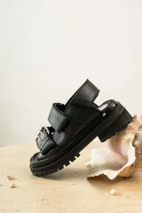 Sandalias negras de cuero con diseño de plataforma dentada, tiras ajustables con hebillas metálicas y detalle de tachas plateadas en el lateral de la suela.